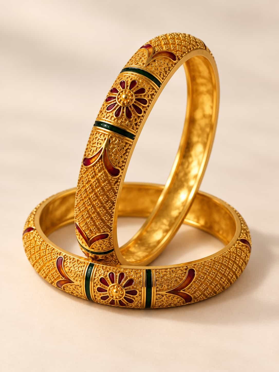 Angled view of Zariya microgold kada bangles showing textured gold-look surface with red and green enamel details